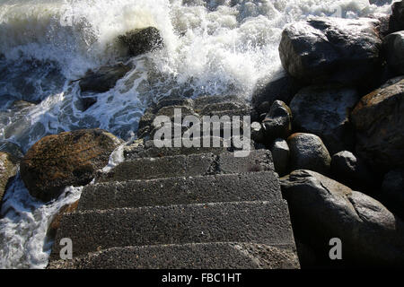 Ocean vagues se brisant sur les rochers ensoleillés et survécu à l'escalier menant à l'eau. Les Beaux-arts,choix, l'espoir, le temps Banque D'Images