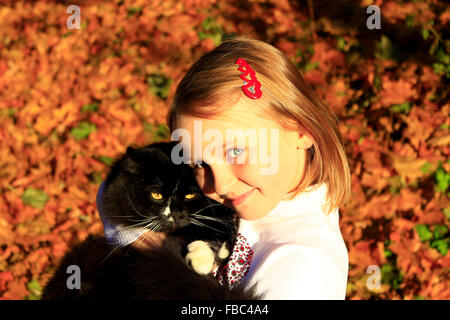 Petite fille embrassant avec son chat noir en automne Banque D'Images