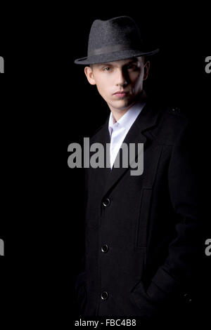 Portrait de jeune homme confiant beau élégant sur fond noir, portant un chapeau et manteau, studio shot low key Banque D'Images