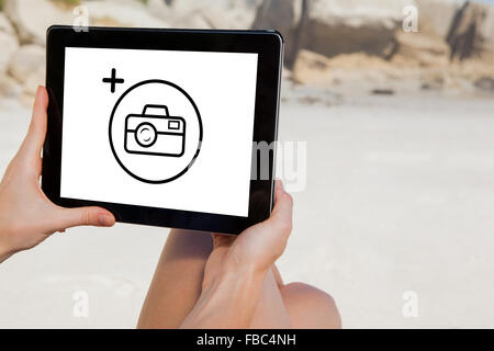 Image composite de femme assise sur la plage à l'aide de tablet pc Banque D'Images