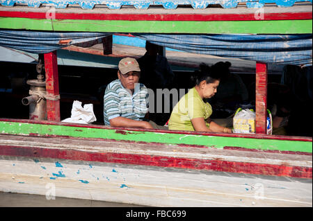 Un homme et une femme birmane s'asseoir dans une cargaison de bois bateau sur les rives de la rivière Ayeyarwady au Mandalay Myanmar Birmanie Banque D'Images