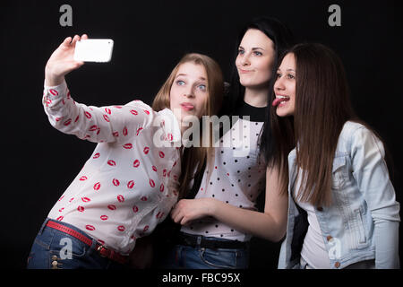 Groupe des belles copines tirant funny faces, en tenant, selfies self-portrait with smartphone, meilleurs amis happy smiling tog Banque D'Images