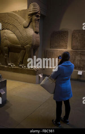 Visiteur musulmane prend une photo avec un smartphone d'une paire de esprits protecteurs assyrienne - un Ugallu - ou grand lion, précédé par ce qui peut être une maison de Dieu au sujet de 700-692BC de l'ancienne ville de Ninive, Banque D'Images