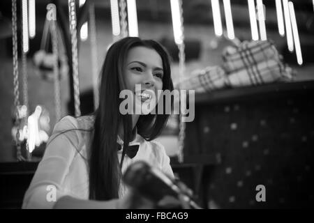 Photo en noir et blanc de belle cheerful brunette girl barman de servir de l'alcool boire au comptoir du bar, le coulage de verre à partir du bot Banque D'Images