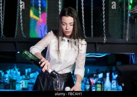 Barman belle brunette girl wearing chemise blanche et noeud papillon noir, service de l'alcool boire au comptoir du bar, tenue en bouteille Banque D'Images