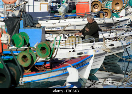 La réparation des filets de pêche pêcheur dans entre les bateaux de pêche traditionnels en bois. Kotsinas quay, limnos island, Grèce. Banque D'Images