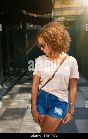 Young African American city girl. Elle porte tenue décontractée, lunettes de soleil et à la recherche vers le bas. Banque D'Images