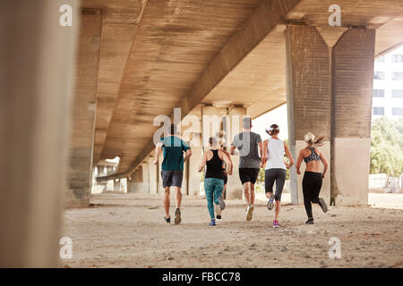 Vue arrière d'une jeunesse saine fonctionnant ensemble. Running club en formation de groupe sous un pont dans la ville. Banque D'Images