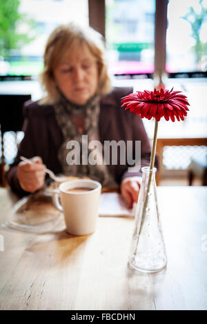 Dame d'affaires de manger, de boire et de la lecture dans un restaurant à Liverpool avec une fleur comme une décoration de table Banque D'Images