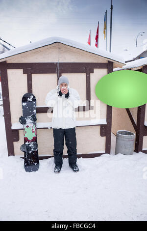 Snowboarder savourer une tasse de café chaud qu'il est à côté de son conseil devant une cabane sur un centre de ski alpin Banque D'Images