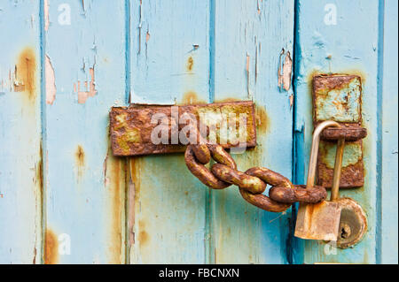 Une chaîne rouillée sur une porte en bois patiné avec un cadenas. Banque D'Images