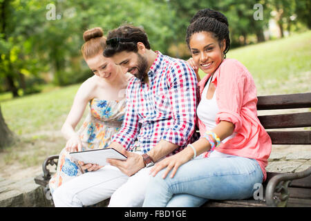 Amis multiraciale, assis sur le banc avec tablet Banque D'Images