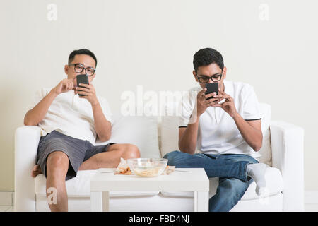 Amis assis sur un canapé et jouer sur leur téléphone à la maison. Banque D'Images