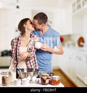 Homme affectueux baiser sa petite amie tout en coupant le pain pour le petit-déjeuner dans la cuisine Banque D'Images