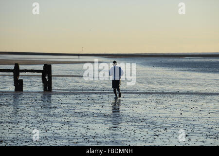 Un homme reprend sa course le long du sable humide à marée basse à l'East Beach à Littlehampton, West Sussex, Angleterre. Banque D'Images