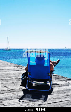 Un homme méconnaissable au soleil dans une chaise longue sur un quai en bois dans la mer Méditerranée, sur la côte d'Azur, France Banque D'Images