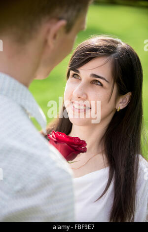 Les amateurs de couple sur une date de réunion, l'accent sur smiling young woman receiving bliss avec rose rouge comme cadeau de son petit ami Banque D'Images