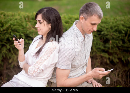 Couple sur banc de parc maintenant des téléphones portables dans les mains, à l'aide de l'app, absorbé dans la communication téléphonique, pas ta Banque D'Images