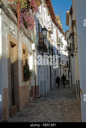 Petite rue latérale dans l'Albaicin à Grenade en Espagne avec des gens à monter une pente raide de la rue pavée avec des maisons blanches et des lampes Banque D'Images