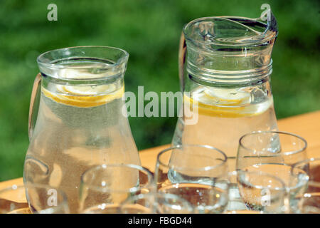 Les deux carafes d'eau fraîche aromatisée au citron et les verres sur une table dans le jardin Banque D'Images