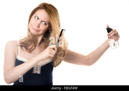 Funny fronçant young attractive blonde woman holding vaporisateur coiffeur, coiffure ciseaux et peigne, mécontent de sa hai Banque D'Images