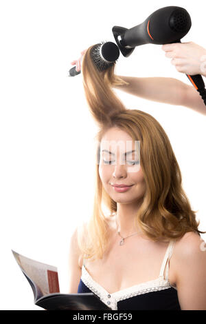 Portrait of young smiling brunette woman sitting at salon de lecture du magazine de mode, ayant son style de cheveux avec hai Banque D'Images