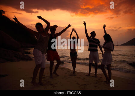 Groupe de personnes à faire la fête sur la plage au coucher du soleil Banque D'Images