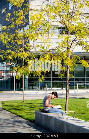 Student sitting on bench et de la lecture en dehors de Alan Turing, l'Université de Manchester, UK Banque D'Images