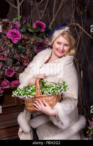 Assez grande taille femme avec panier de fleurs de printemps en manteau avec fourrure sombre sur fond de fleurs Banque D'Images