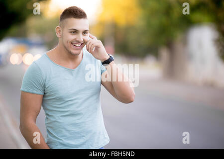 Portrait of happy smiling bonne recherche jeune mec vêtements décontractés en marchant dans la rue, holding mobile phone, à l'aide de smar Banque D'Images