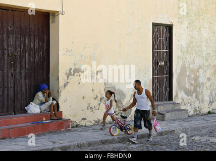 Père et fille marcher passé vieux pauvre femme mendiant dans la rue, Regla, Cuba Banque D'Images