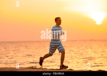 Mode de vie sain : beau jeune homme travaillant sur l'extérieur, fonctionne rapidement sur la rive de sable au coucher et au lever du soleil Banque D'Images