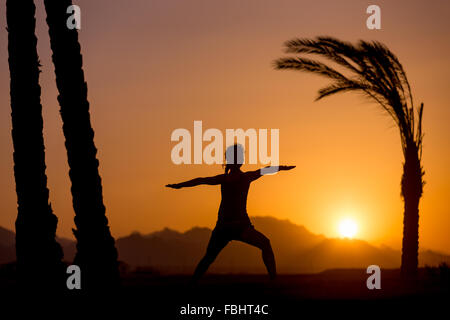 Silhouette de jeune femme pratiquant le yoga ou Pilates au coucher et au lever du soleil dans un beau lieu tropical avec des montagnes et palm Banque D'Images