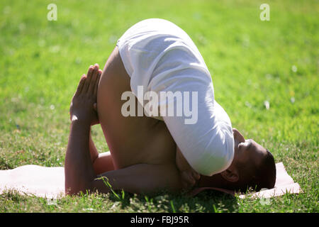 Les jeunes Indiens attrayant homme travaillant sur le mat sur pelouse au parc, faire pindasana dans sarvangasana, variation de la posture de l'embryon, fu Banque D'Images