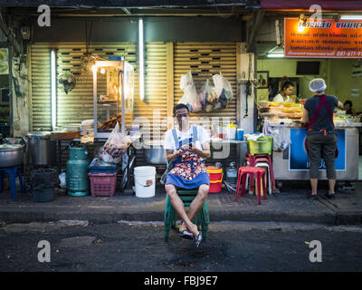 Bangkok, Bangkok, Thaïlande. 17 Jan, 2016. Un stand alimentaire vendeur vérifie son smart phone pendant qu'il attend pour les clients, sur Sukhumvit Soi 38, l'un des plus célèbres domaines de l'alimentation de rue à Bangkok. Les chariots et les petits restaurants le long de la rue ont été populaires auprès des touristes et les thaïlandais pour plus de 40 ans. La famille qui est propriétaire du terrain le long de la di a récemment décidé de vendre à un promoteur de condominiums et de ne pas renouveler les baux des propriétaires de restaurant. Plus de 40 restaurants et de chariots devront fermer. La plupart des restaurants sur la rue fermée durant l'été 2015. Le rester Banque D'Images