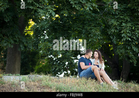 Portrait of beautiful happy young couple in love se reposant sous les arbres d'érable, se regarder, assis ensemble sur g Banque D'Images