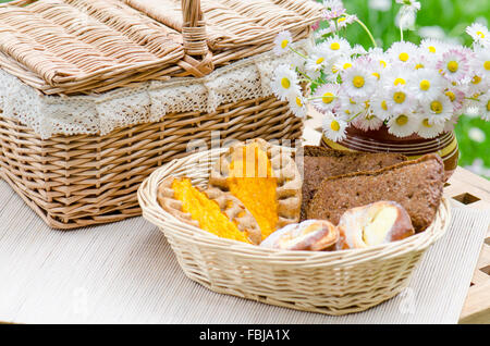 Petits pains dans un panier en osier et un bouquet de fleurs Banque D'Images