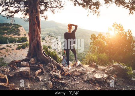 Jeune femme debout sur la montagne près de vieil arbre au coucher du soleil. Paysage naturel d'été Banque D'Images