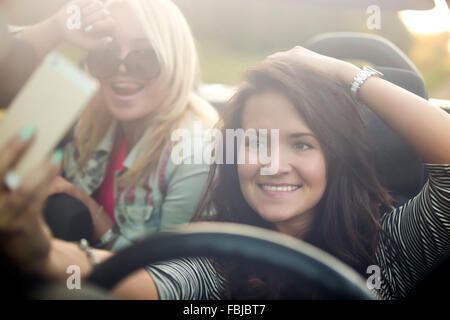 Deux belles jeunes femmes positives voyageur prenant portrait selfies avec caméra téléphone mobile en voiture, sourire, posant, s'amuser Banque D'Images