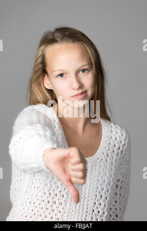 Portrait de malheureux beau casual caucasian girl wearing white chandail tricoté, showing Thumbs down, looking at camera Banque D'Images