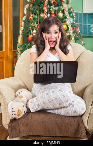 Heureuse Jeune Femme utilisant un ordinateur portable avec l'excitation à la maison , jolie fille en pyjama et chaussons moelleux naviguant sur Lapt Banque D'Images