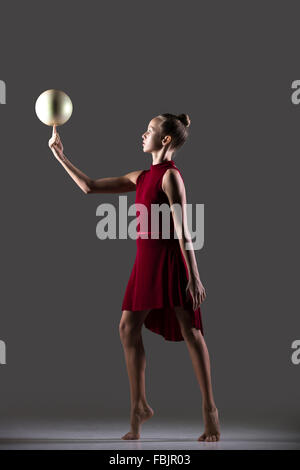 Cool belle jeune femme athlète gymnaste fit en robe rouge vêtements de travail, faisant de l'exercice de gymnastique rythmique Banque D'Images