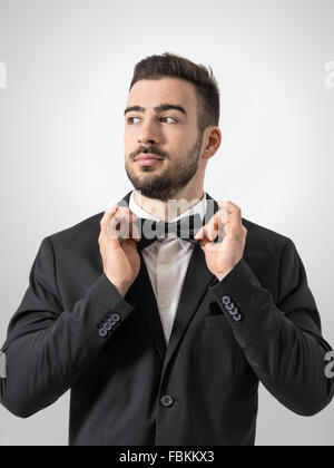 Cool man adjusting détendue confiant à la cravate d'arc de là. Portrait désaturée sur fond gris avec vignette retro studio