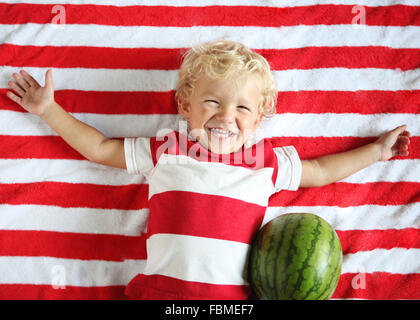 Smiling boy lying on blanket à rayures avec watermelon Banque D'Images