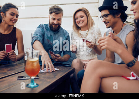 Groupe d'amis se détendre et jouer aux cartes ensemble. Les jeunes traînant autour d'une table lors d'une partie de la lecture d'un Banque D'Images