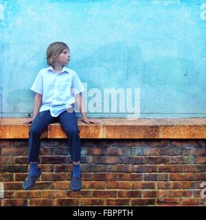 Teenage Boy Wearing Blue shirt et jeans Sitting on Wall