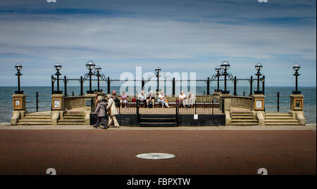 Les personnes âgées assis sur des sièges et en passant devant le kiosque le long de la promenade de Llandudno Banque D'Images