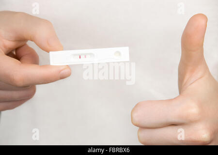 Jeune femme tenant dans ses bras en plastique rapide test de grossesse positif avec deux rayures suite et showing Thumbs up Banque D'Images