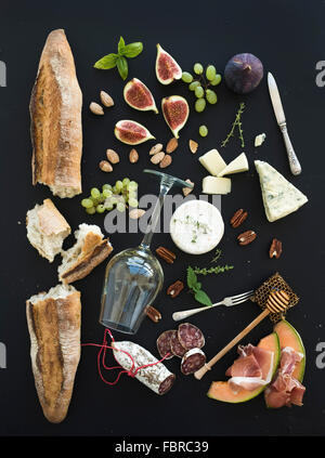 Vin et snack-set. Baguette, verre de blanc, figues, raisins, noix, fromage, viande et divers hors-d'herbes sur noir grunge retour Banque D'Images