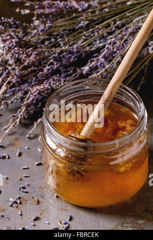 Ouvrir un bocal en verre de miel liquide et le miel d'abeilles avec balancier à l'intérieur et à l'ensemble de la lavande sèche plus vieux rust surface métallique. Rus Banque D'Images